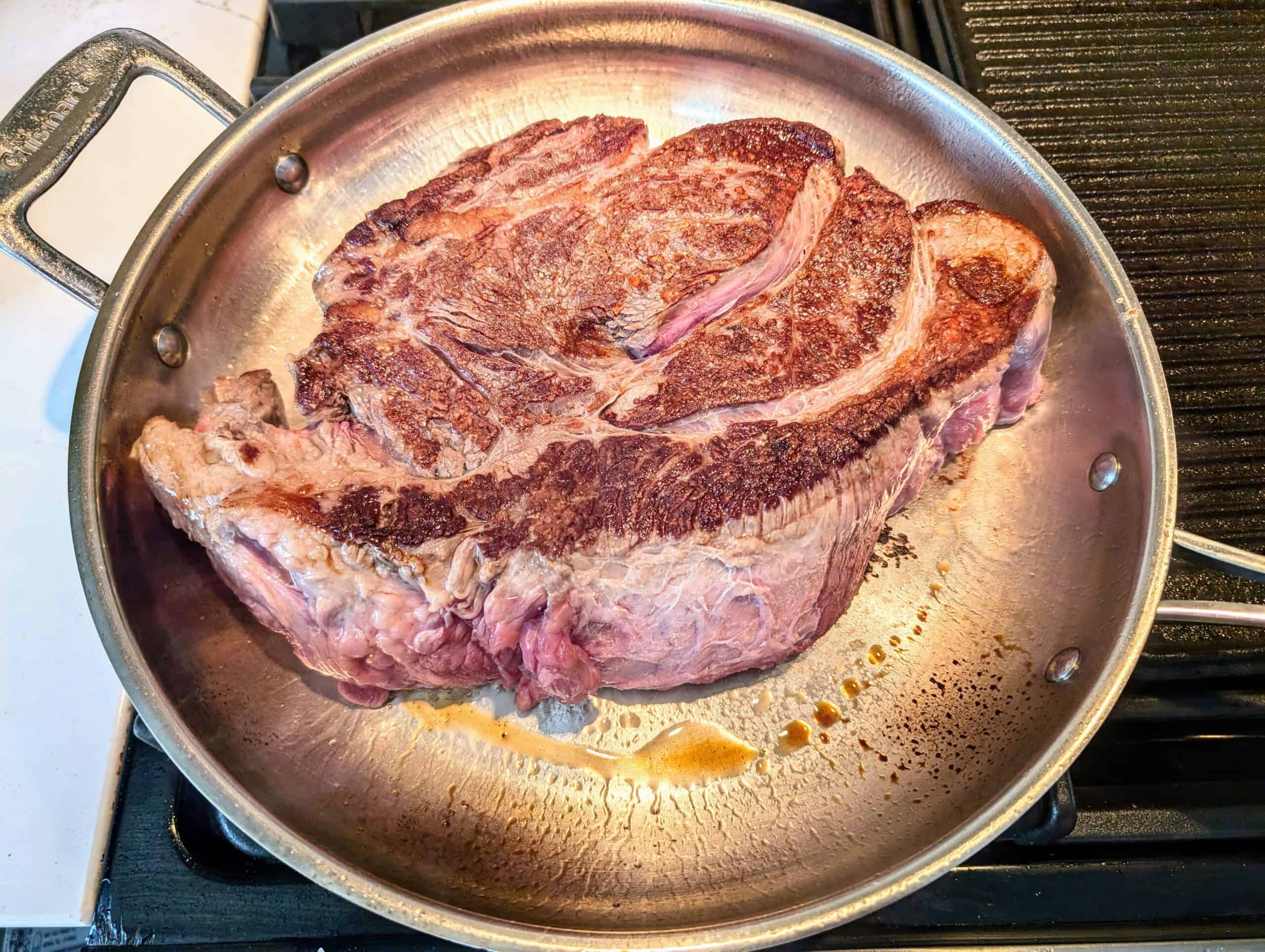 a skillet with a chuck roast being seared in pork fat 