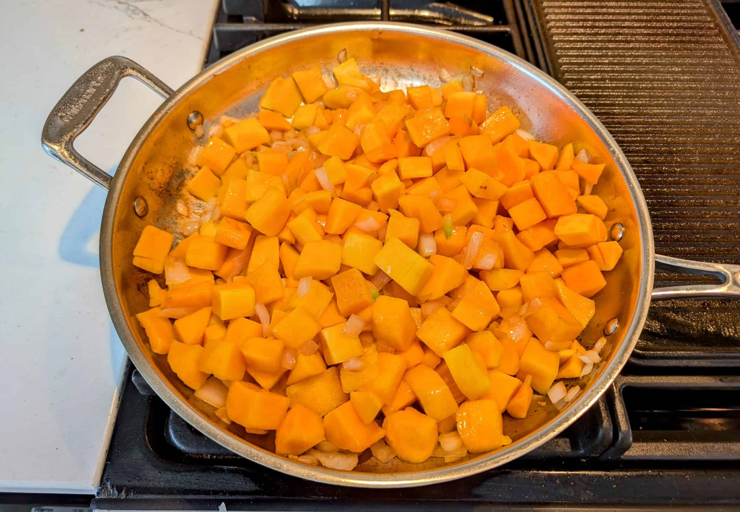 Stove top skillet with sauteed onions and butternut squash in a skillet with pork fat 